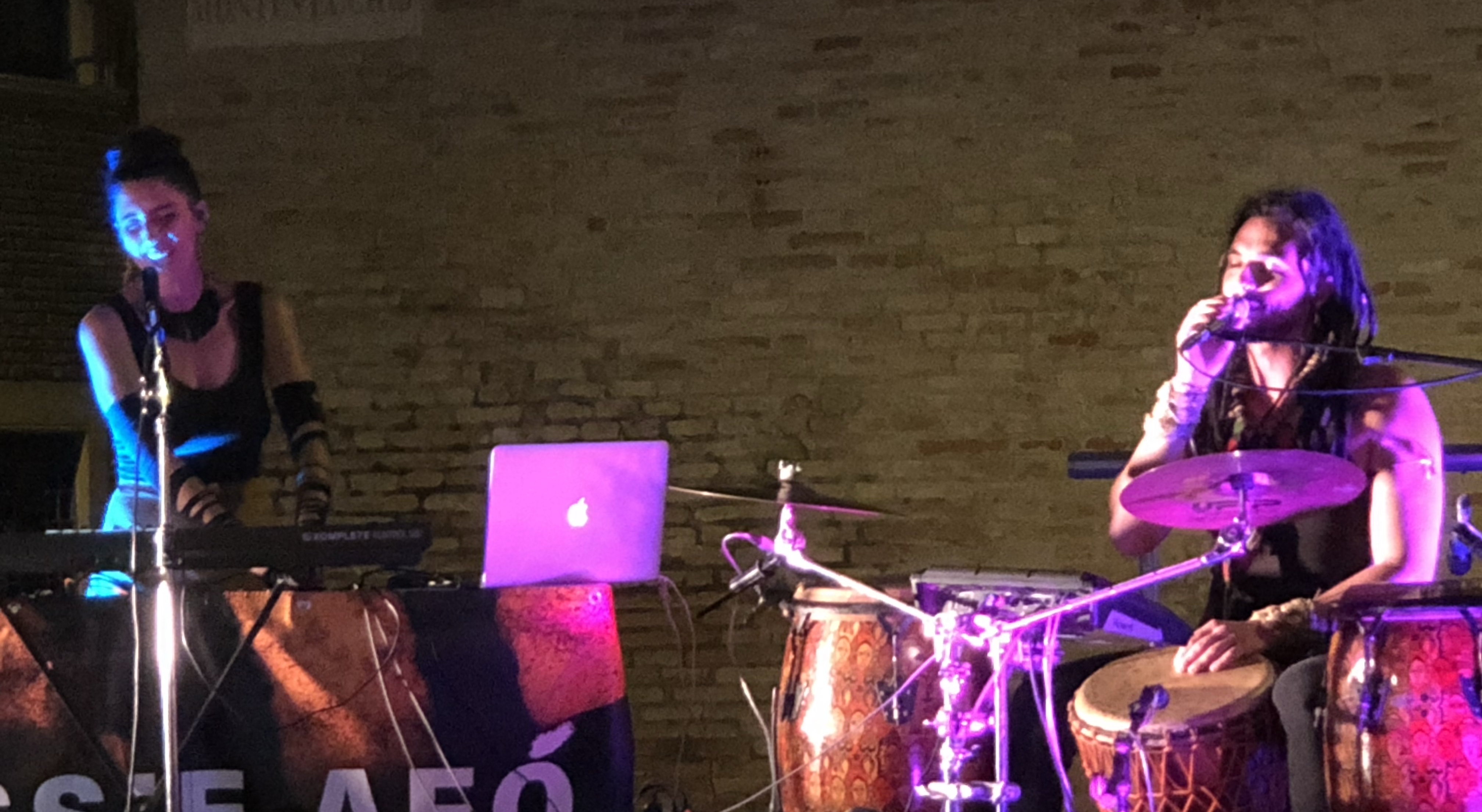 A sinistra tastierista/vocalist femmina, a destra percussionista/vocalist maschio, in mezzo un Mac